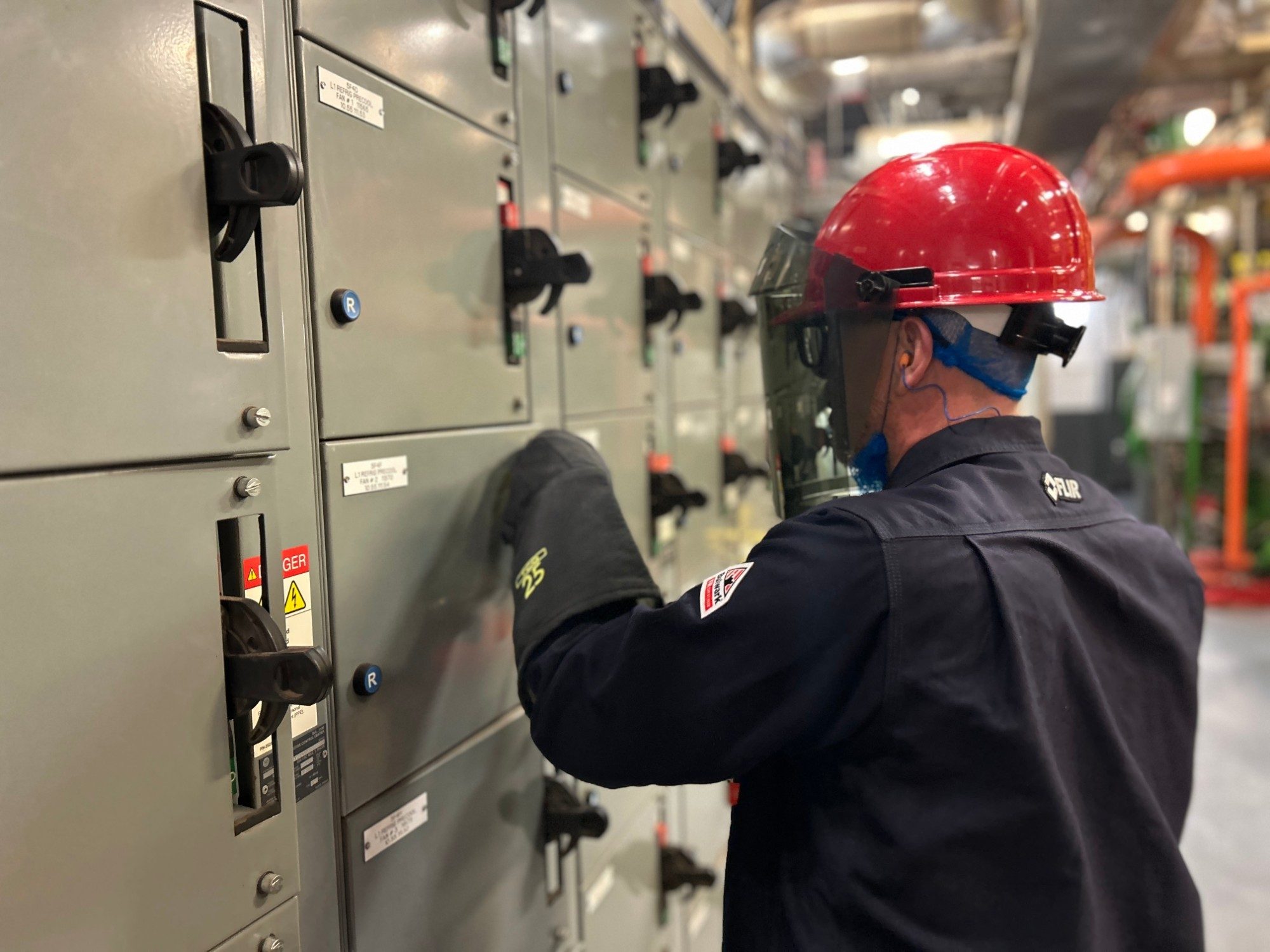 Technician in an arc-rated face shield and gloves operating a motor control centre